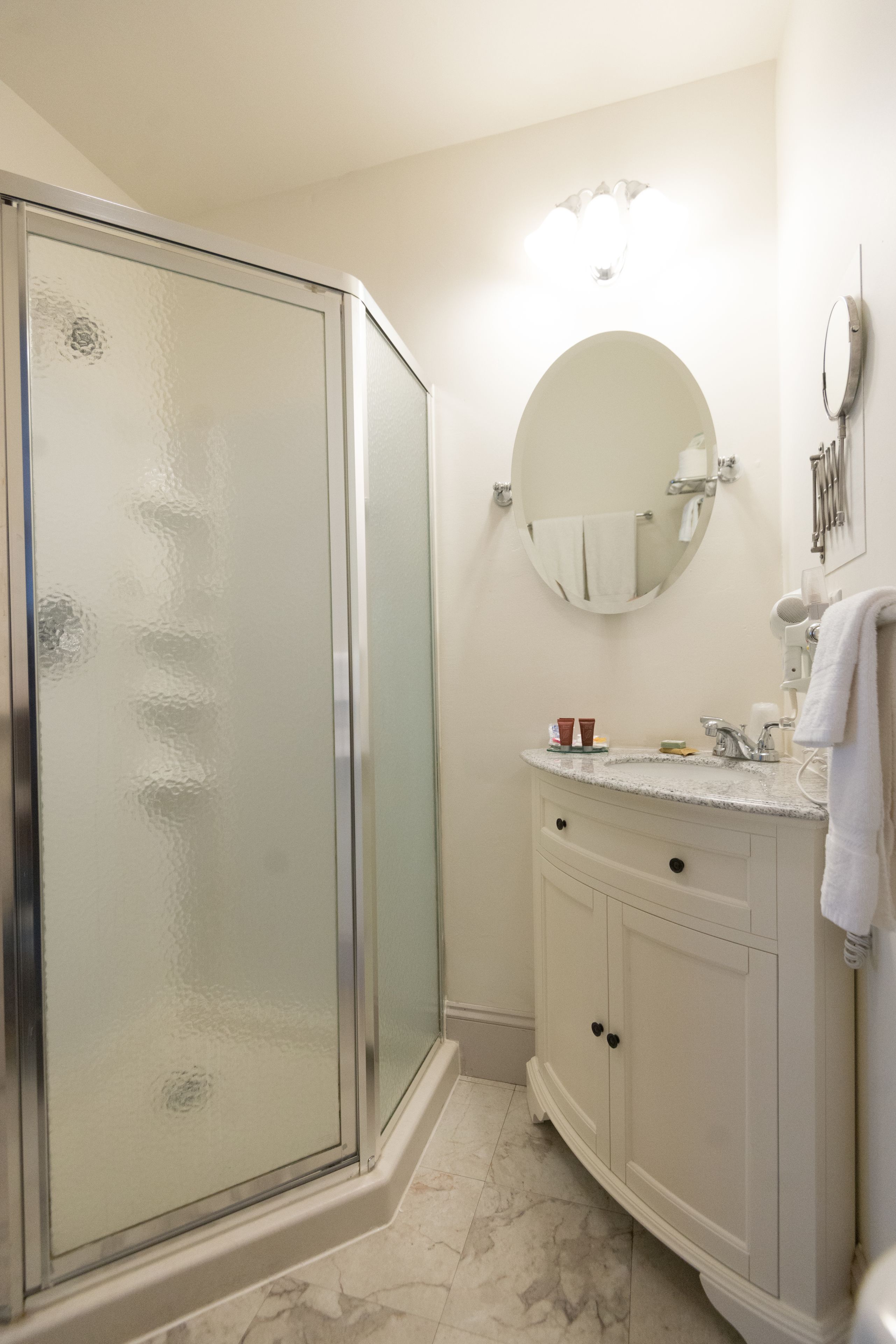 Un baño con ducha de vidrio, un espejo redondo, un lavabo con encimera y un mueble con cajones.