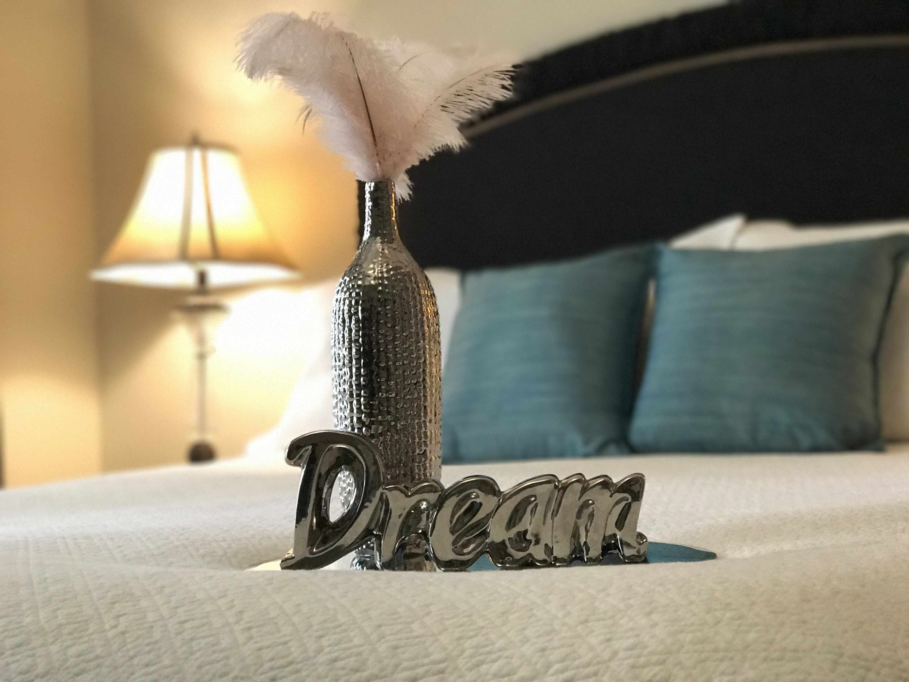 Een bed met een decoratieve fles en veer, en het woord 'Dream' erop.