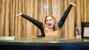A person standing at a reception desk with arms raised, in front of a wooden curtain backdrop. - Camas Boutique Hotel (Camas)