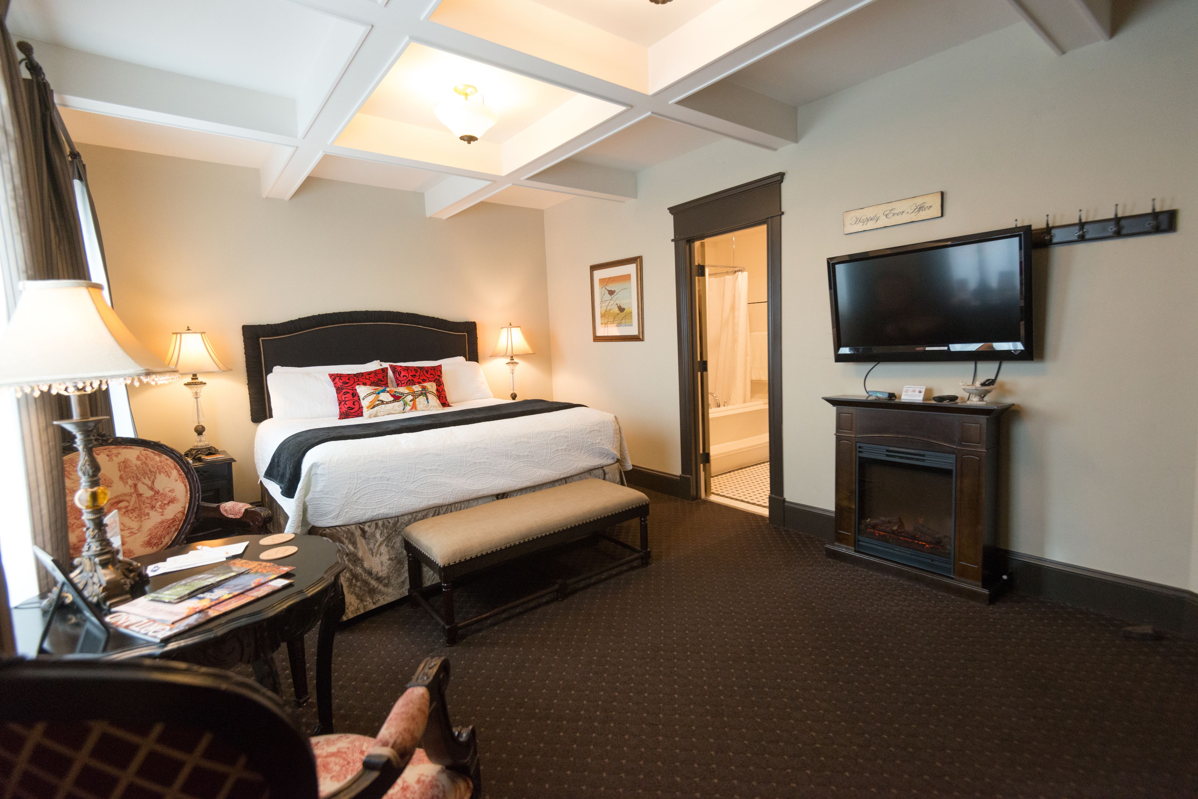 Une chambre d’hôtel comprenant un lit, des lampes de chevet, une télévision, une cheminée et un bureau avec une chaise.