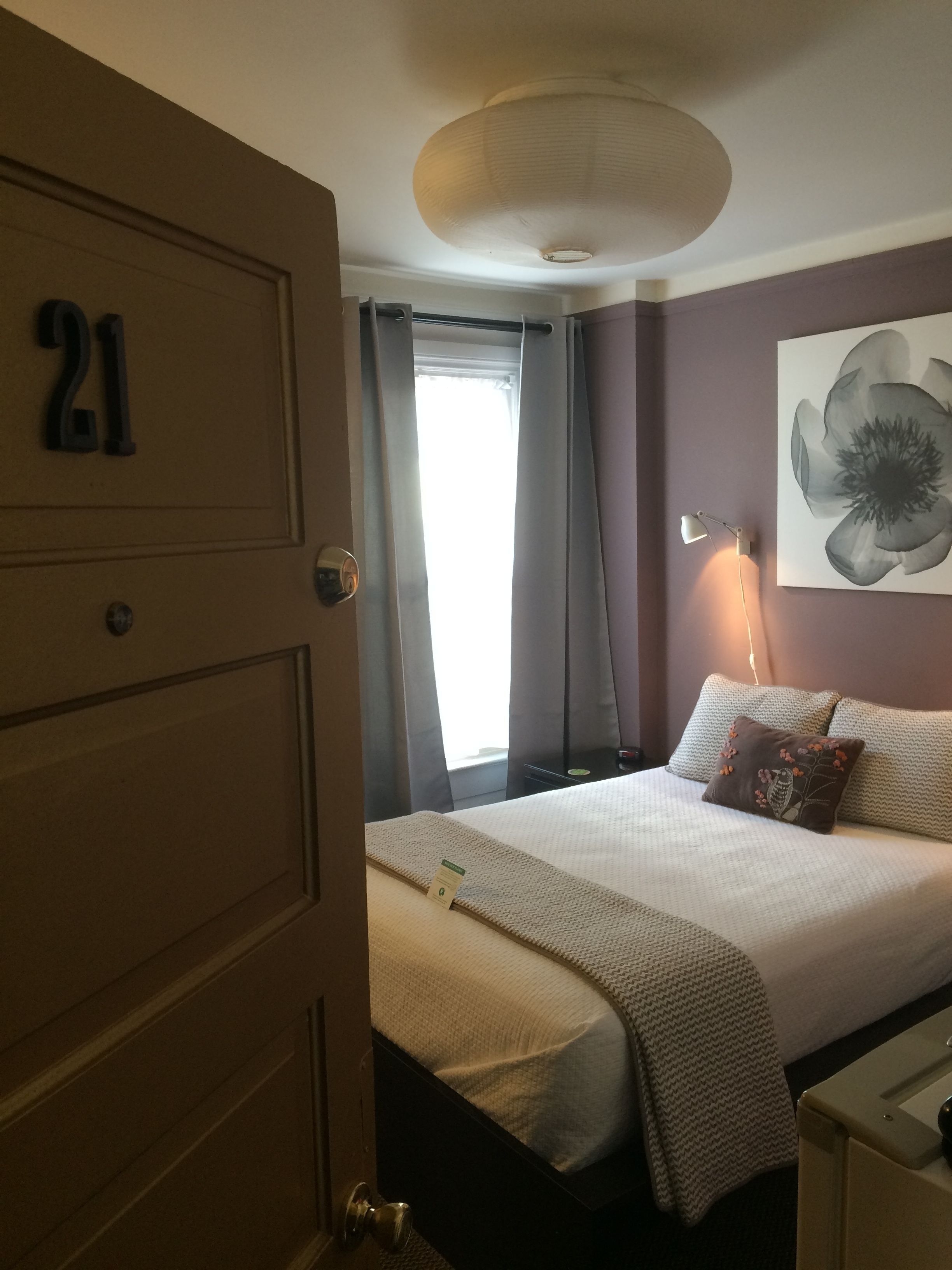 A hotel room with a bed, a nightstand, a lamp, a painting, and a door with the number 21.