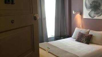 A hotel room with a bed, a nightstand, a lamp, a painting, and a door with the number 21.
