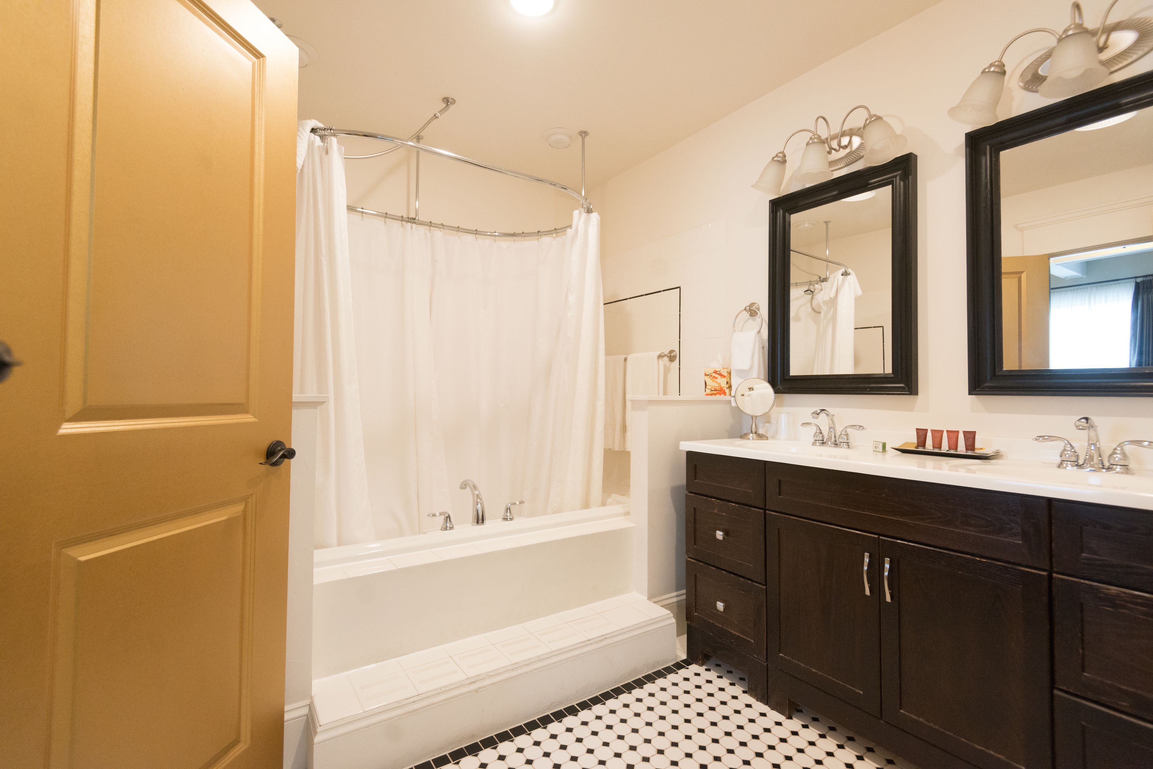 A bathroom with a bathtub, a shower curtain, a sink with a mirror, and a dark wooden vanity.