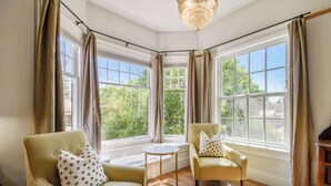 A corner room with two armchairs, a round table, and a view of greenery through large windows. - Cedar Gables Inn (Napa)