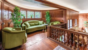 A spacious living room with a curved wooden ceiling, a green sofa, a wooden railing, and two potted plants. - Cedar Gables Inn (Napa)