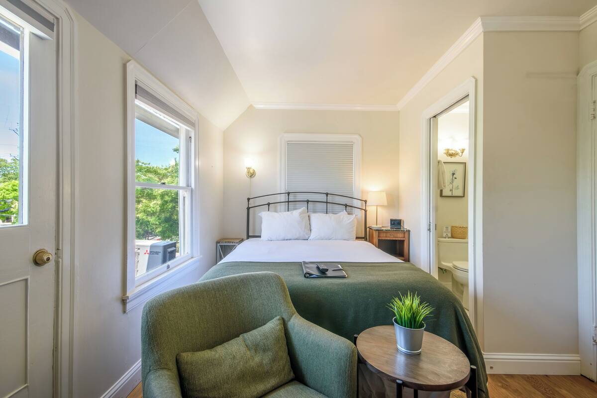 A bedroom with a bed, a chair, a bedside table, and a window.