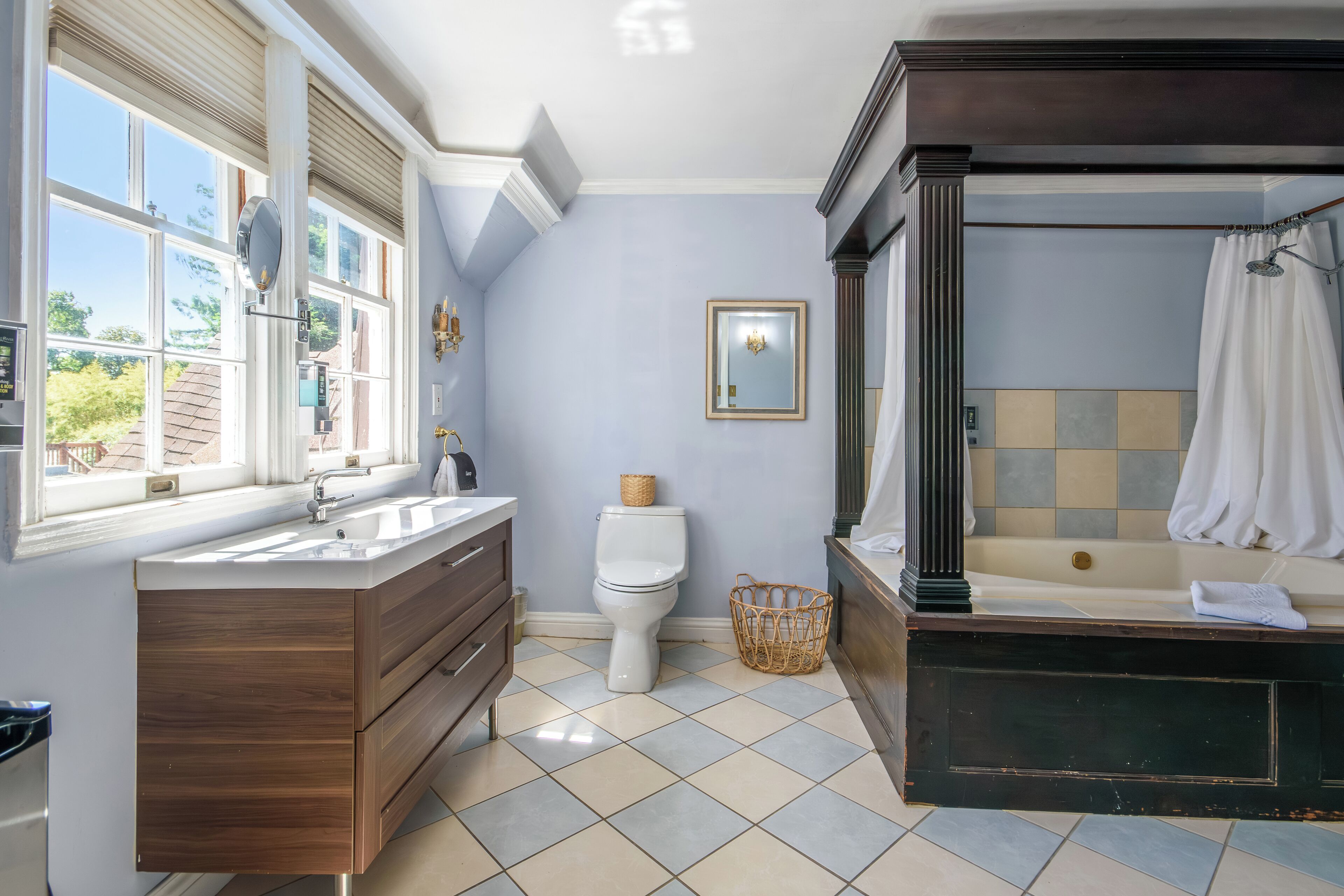 Un baño con tocador de madera, inodoro, bañera y ventana con persianas.