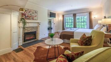 A hotel room with a fireplace, a bed, a dining area, and a view of the outdoors.