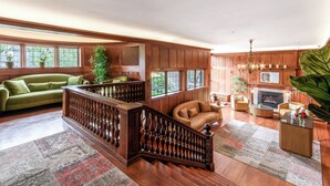 A spacious living room with a wooden staircase, a green sofa, a leather armchair, and a fireplace. - Cedar Gables Inn (Napa)