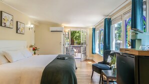 A hotel room with a bed, a desk, a refrigerator, and a view of an outdoor patio. - Cedar Gables Inn (Napa)