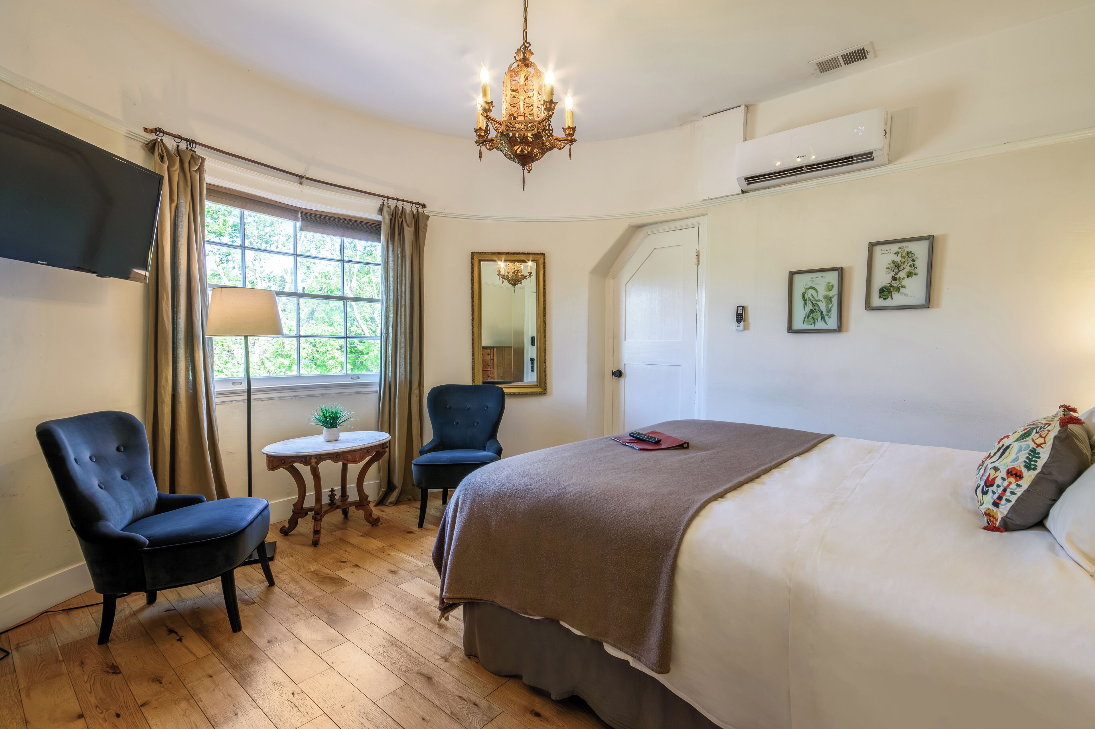 A bedroom with a large bed, a chair, a small table, a mirror, and a chandelier.