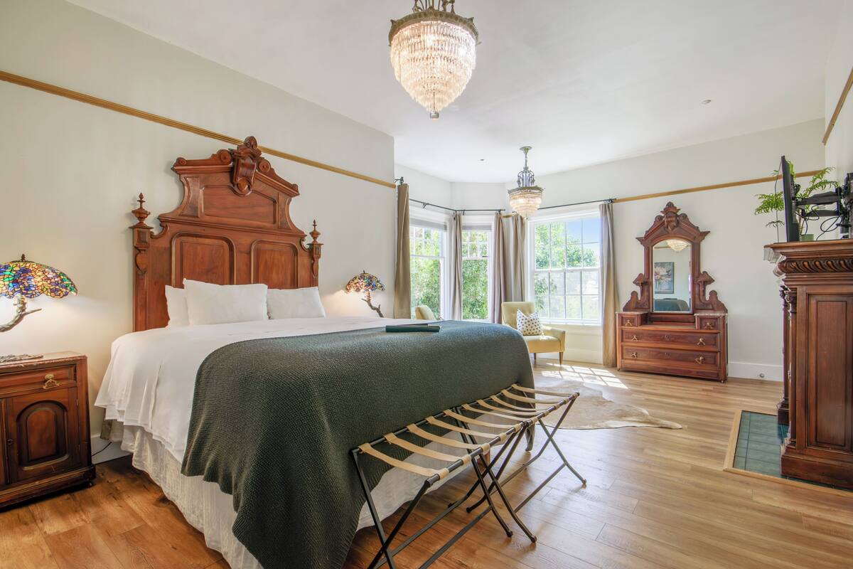 A spacious bedroom with a large bed, wooden headboard, and a chandelier.