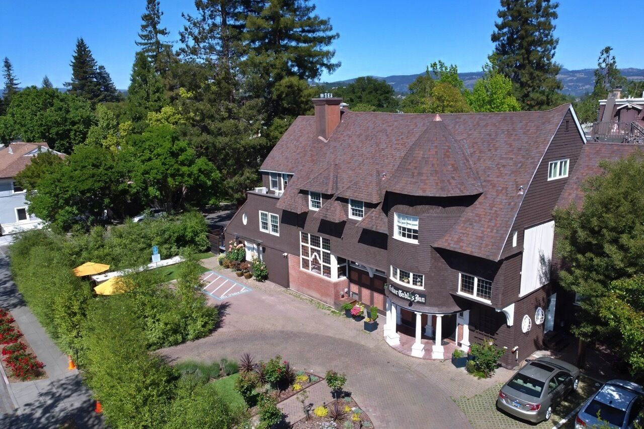 A large, two-story building with a dark brown roof and white trim, surrounded by lush greenery and trees.