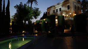 Un edifici amb piscina i una font, envoltat d'arbres i un camí ben il·luminat.