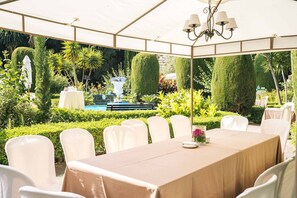 An outdoor dining area with a covered table and chairs, surrounded by well-manicured hedges and a fountain. - Casa de los Bates (Motril)