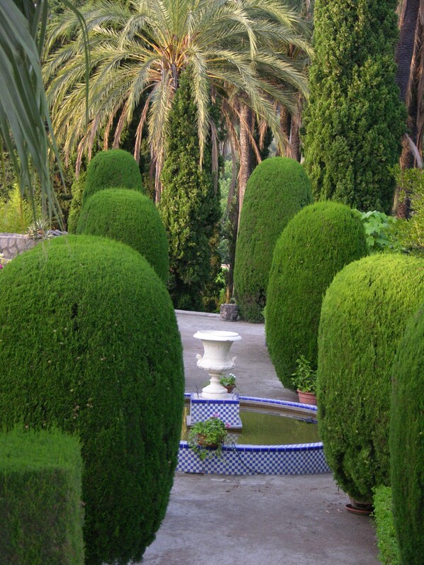 A formal garden with neatly trimmed hedges, a central white urn, and a checkered border around a water feature. - Casa de los Bates (Motril)