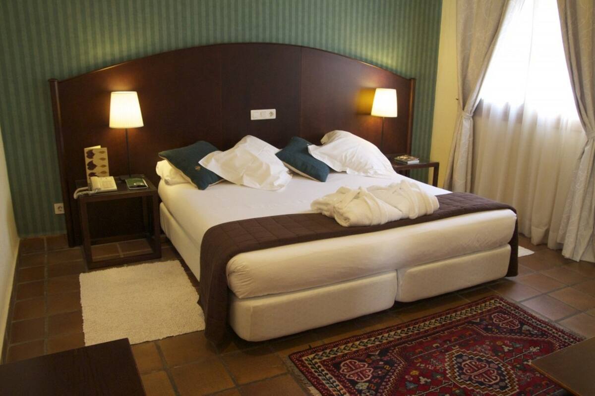 Une chambre d’hôtel avec un grand lit, deux lampes de chevet, un téléphone et un tapis décoratif.