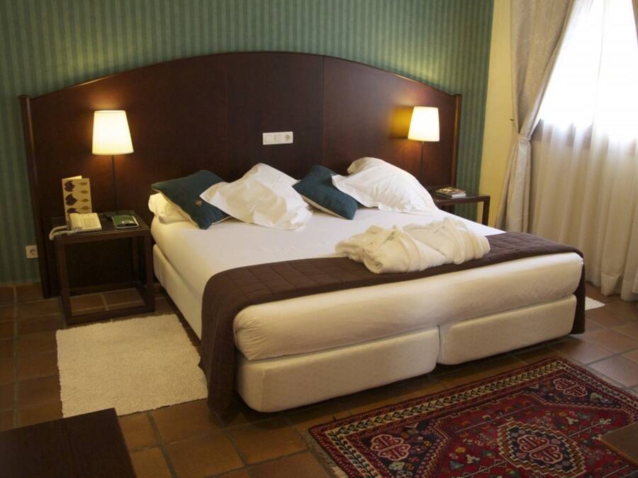 Ein Hotelzimmer mit einem großen Bett, zwei Nachttischlampen, einem Telefon und einem dekorativen Teppich.