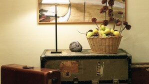 A painting on a wall, a lamp, and a basket of fruit on a trunk. - Rusticae Hotel LEstació (Bocairente)