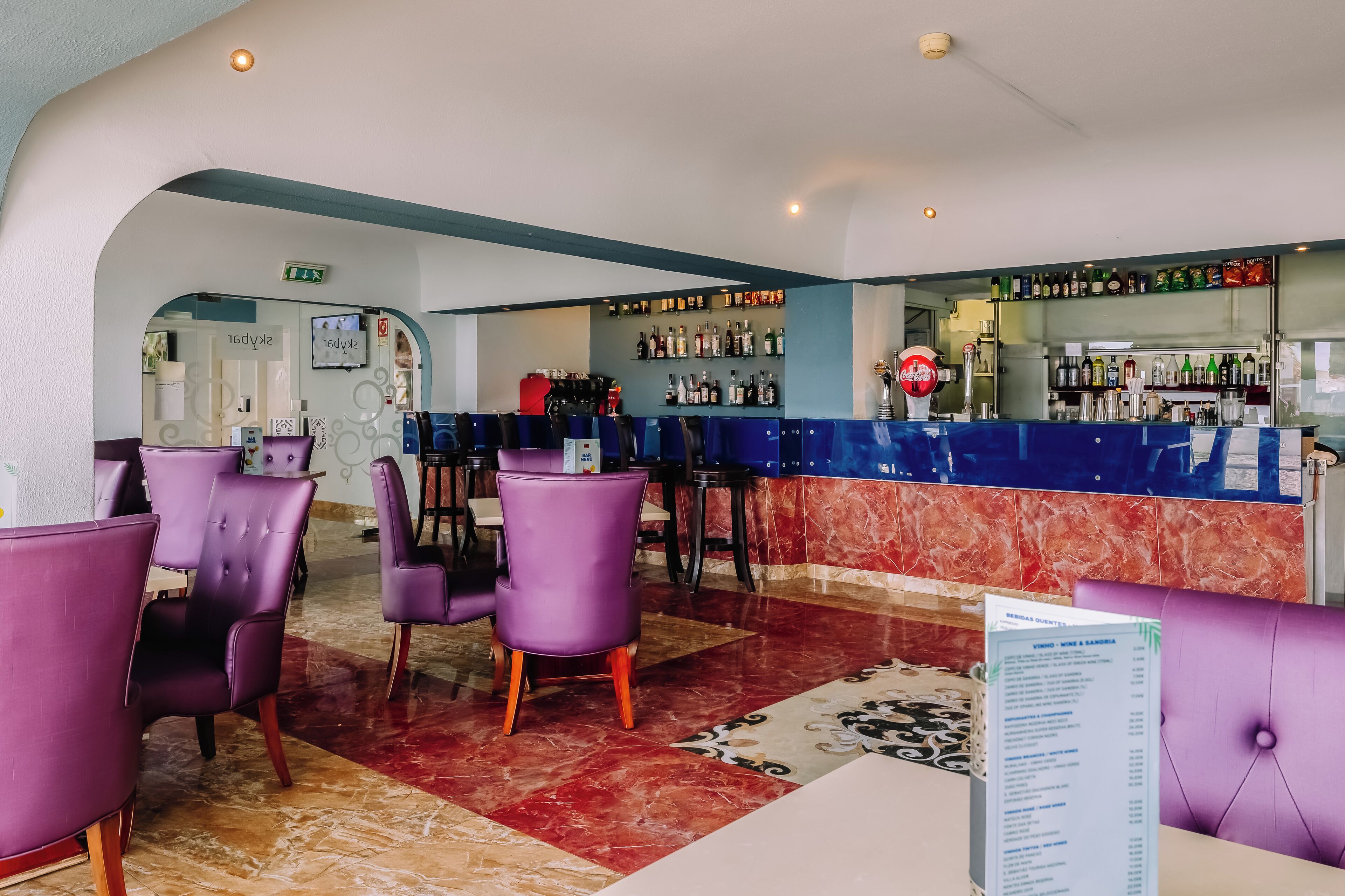 A bar area with purple chairs, a marble floor, and a menu stand.