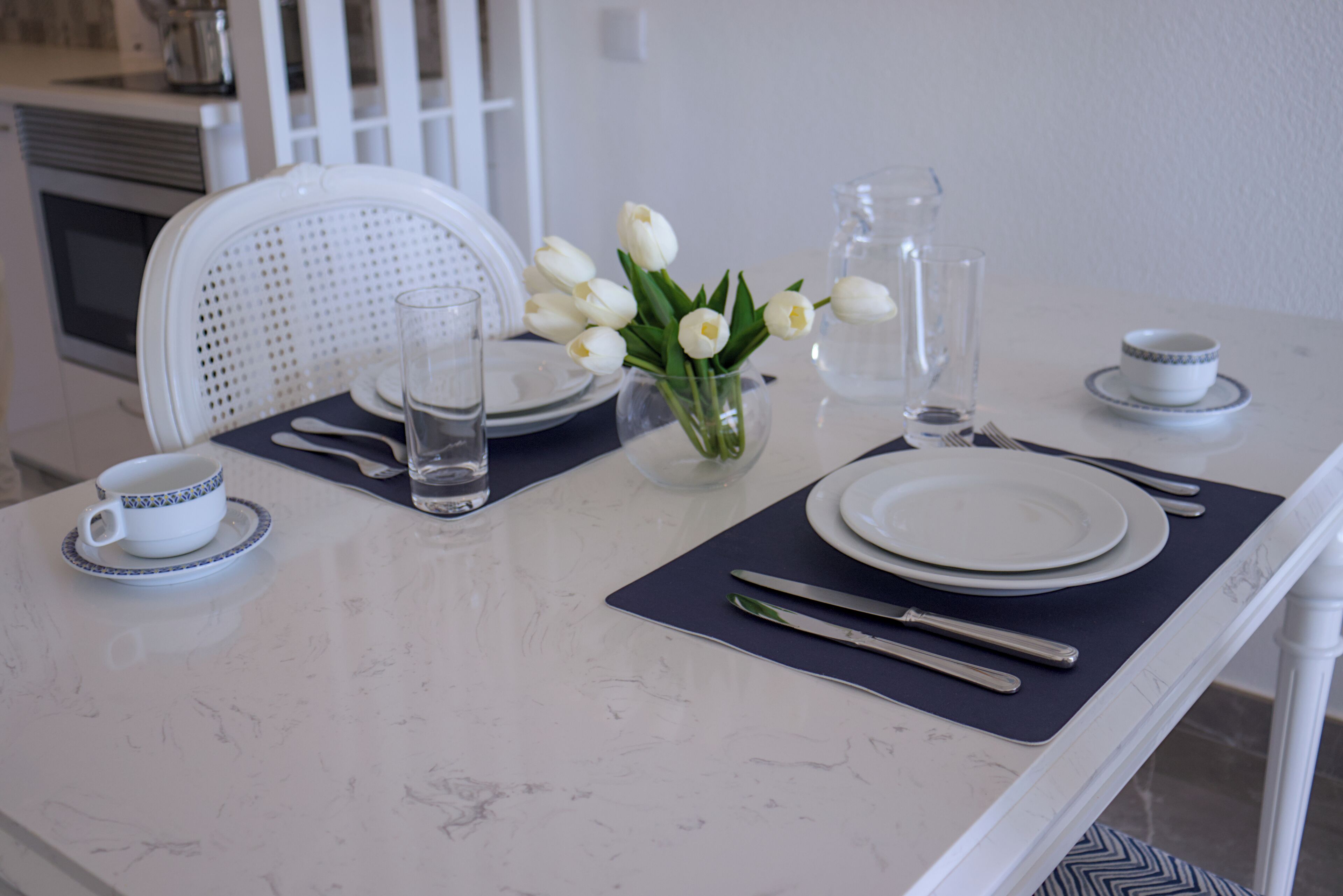 A dining table set with plates, cutlery, a vase of white tulips, and a pitcher of water.