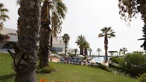 A poolside area with lounge chairs, palm trees, and a building in the background. - Grand Muthu Oura View Beach Club (Albufeira)