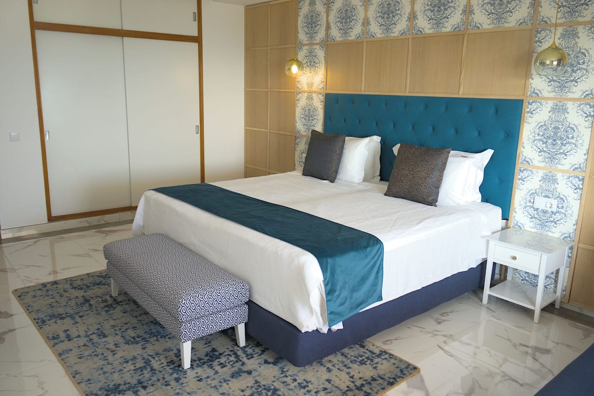 A neatly arranged bedroom with a large bed, a bedside table, a bench, and patterned wallpaper.