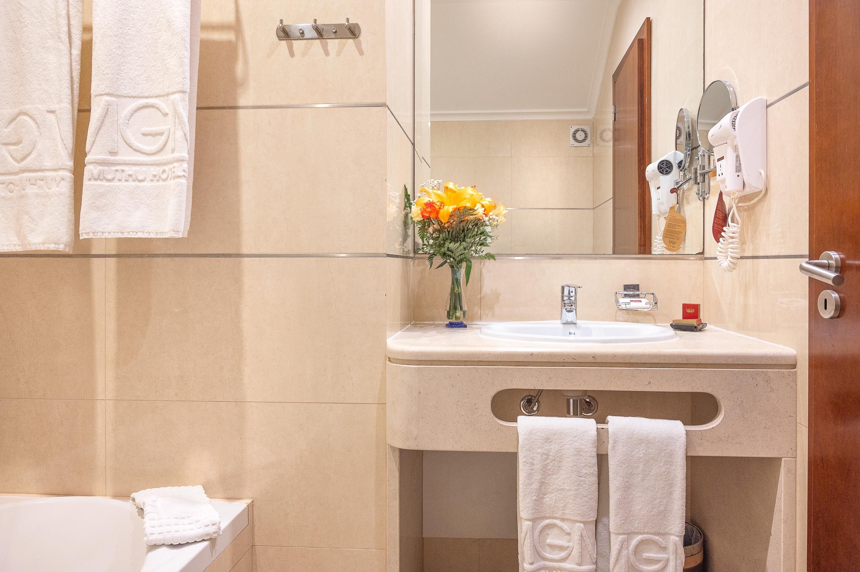Un bagno con un lavabo beige, uno specchio, un portaservizi con asciugamani e un vaso con fiori.