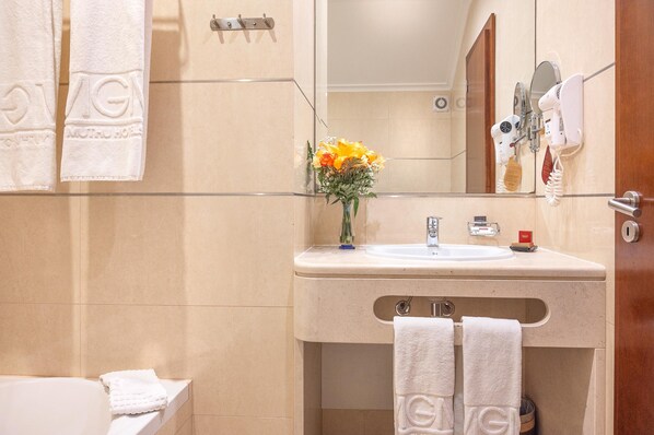 A bathroom with a beige sink, a mirror, a towel rack with towels, and a vase with flowers.