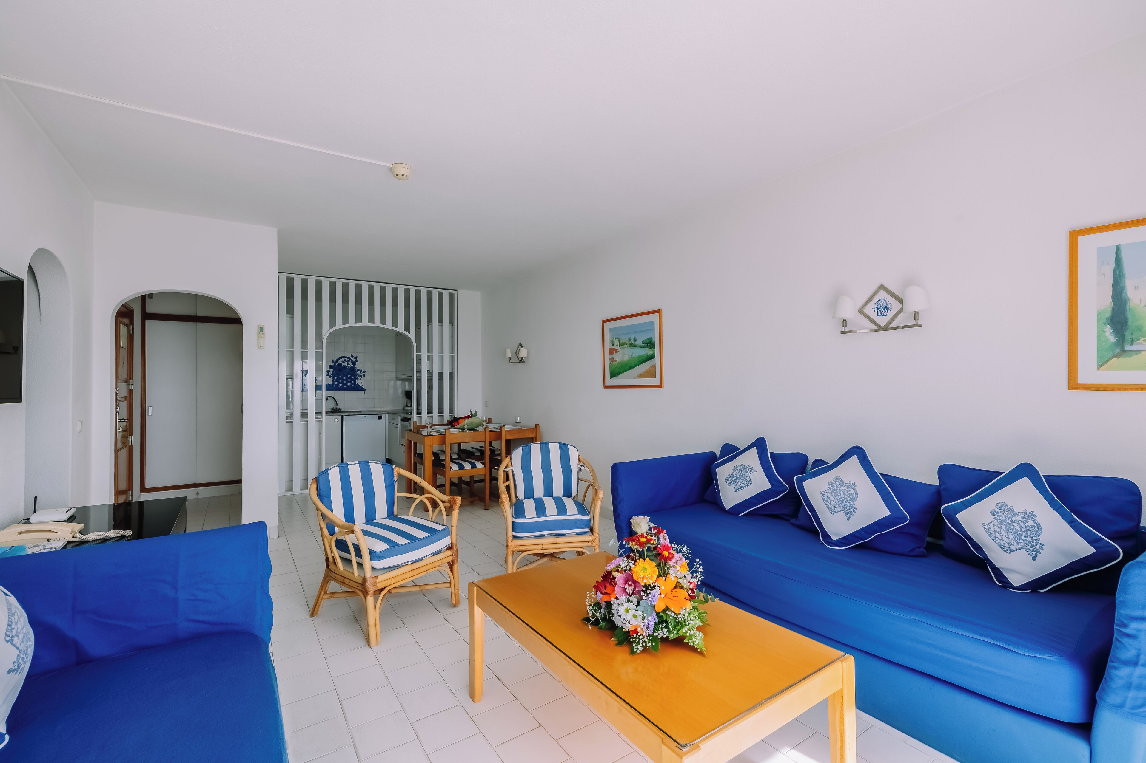 A living room with a blue sofa, striped chairs, a wooden coffee table, and a dining area with a table and chairs.