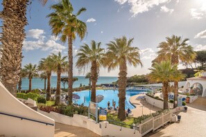 A pool area with palm trees, lounge chairs, and a view of the sea.