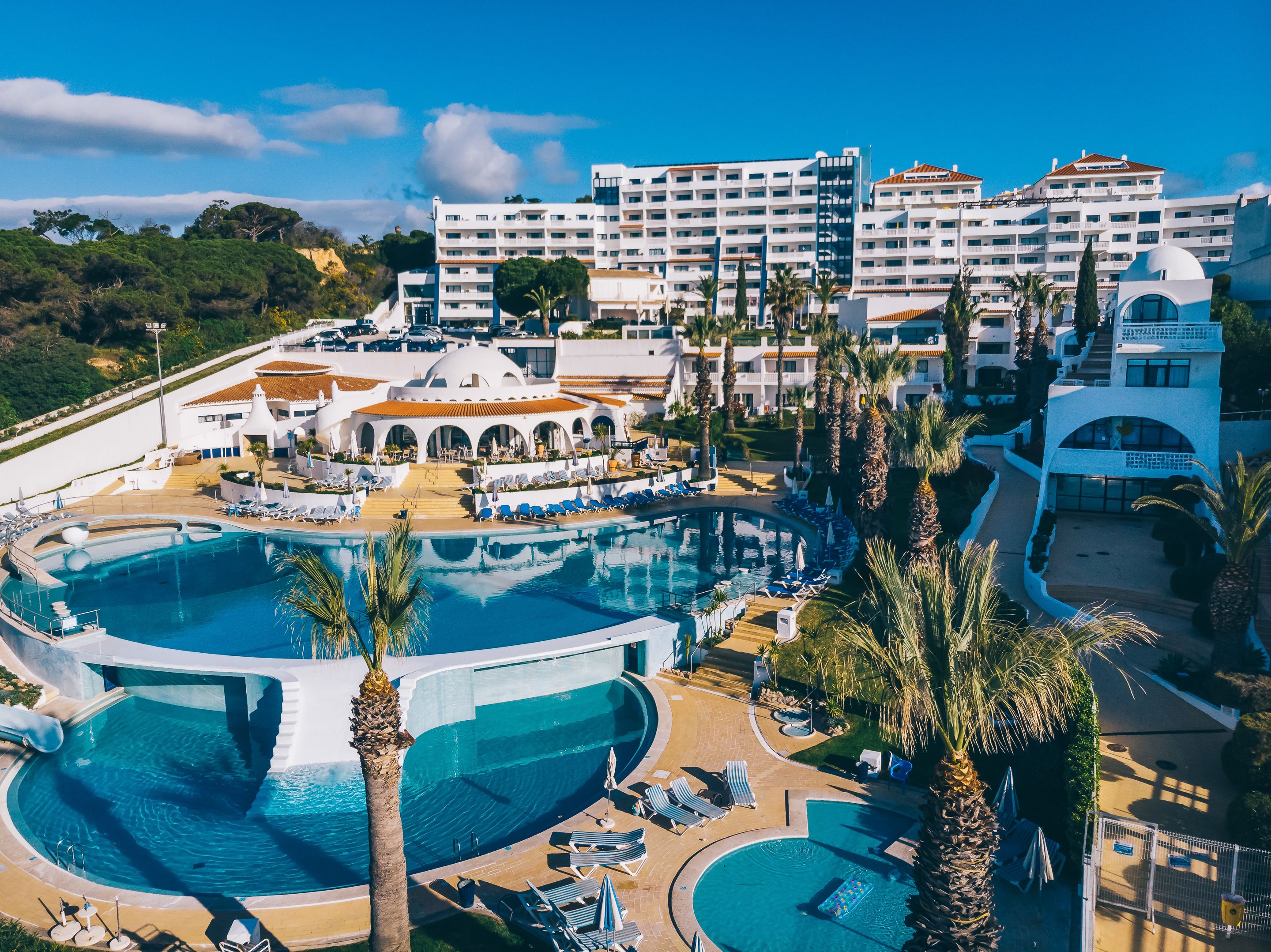 Un resort con varias piscinas, un edificio central con cúpula y un área ajardinada circundante con palmeras.