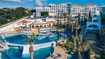 Un resort con varias piscinas, un edificio central con cúpula y un área ajardinada circundante con palmeras.