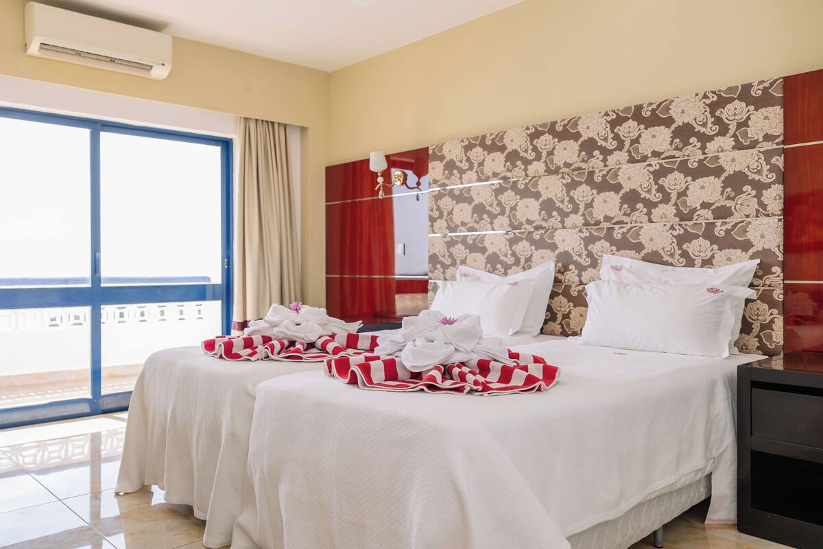A hotel room with a large bed, a nightstand, a window with a view, and a wall with a floral pattern.