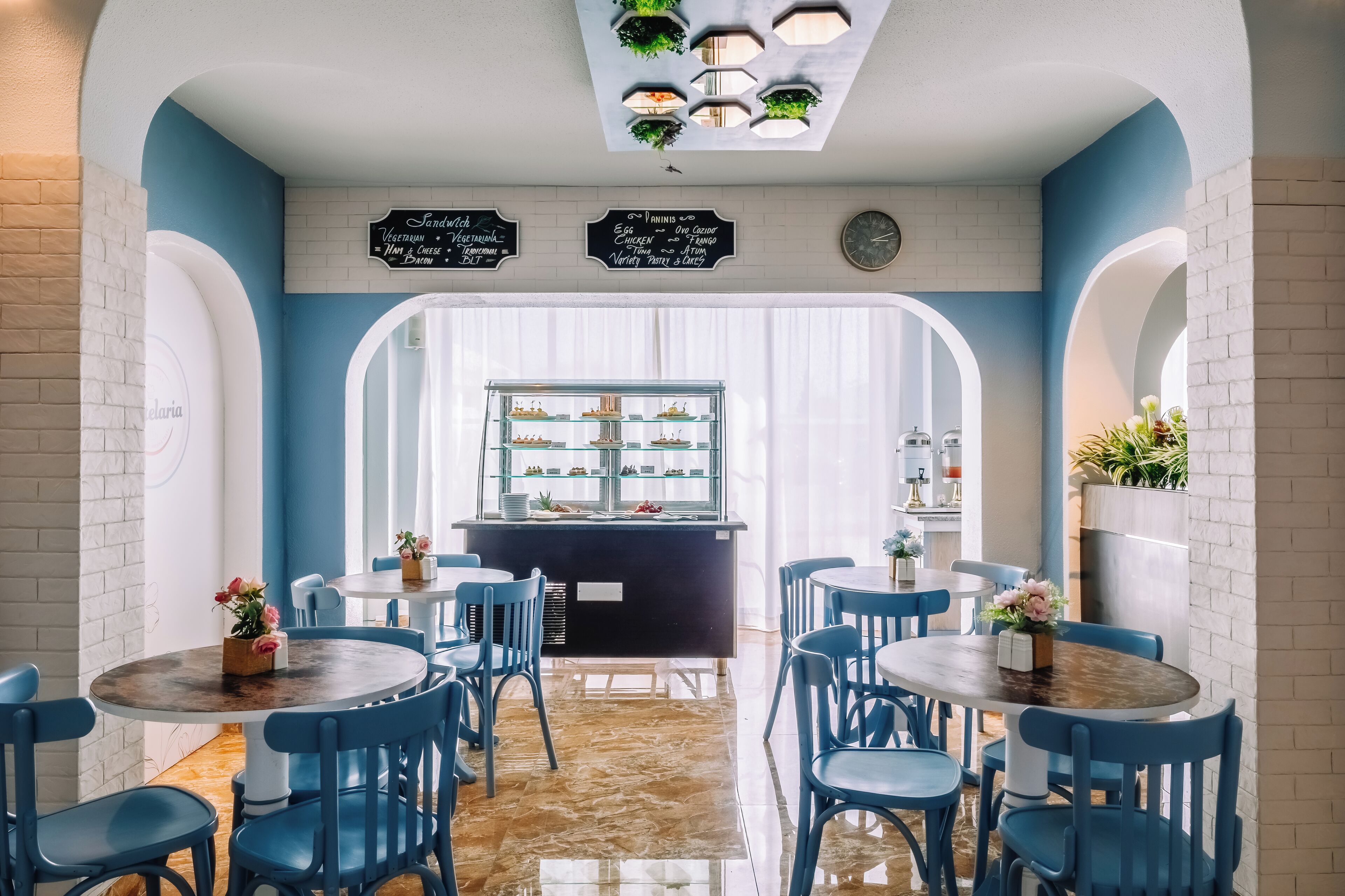 A restaurant with blue chairs and tables, a counter with food displays, and a signboard listing menu items.