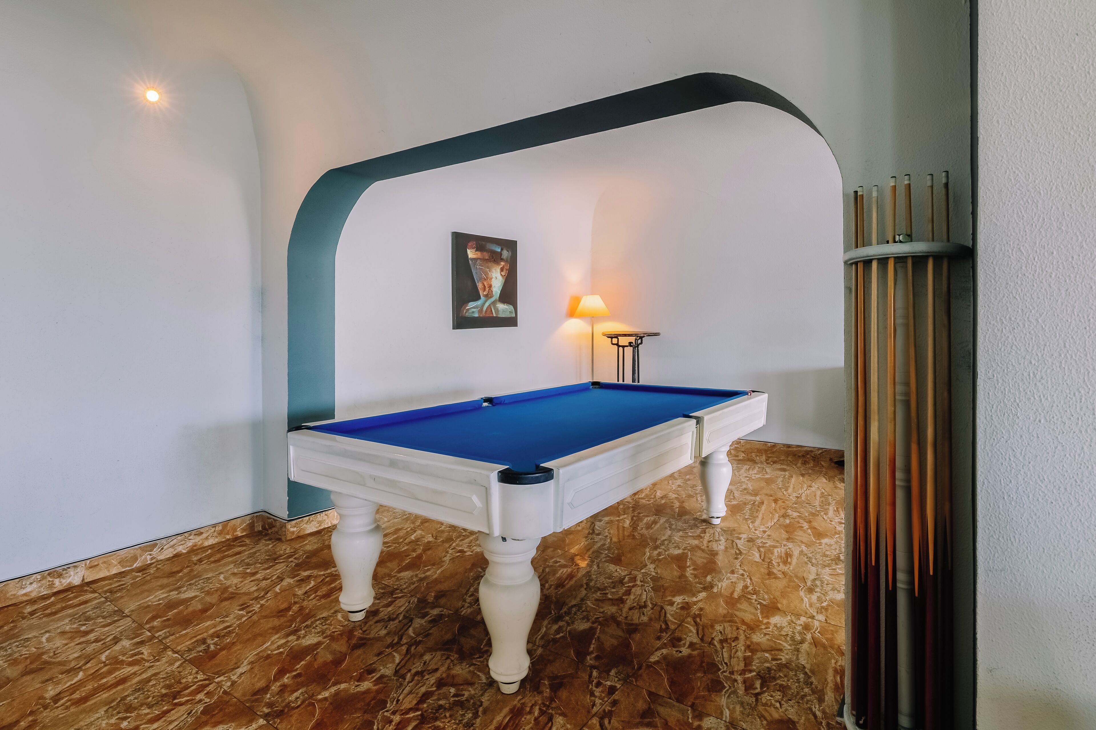 A pool table in a room with a marble floor, a lamp, and a framed picture on the wall.