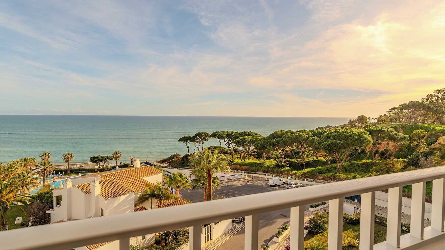 Vista costeira a partir de uma varanda com vista para uma piscina, palmeiras e uma praia.