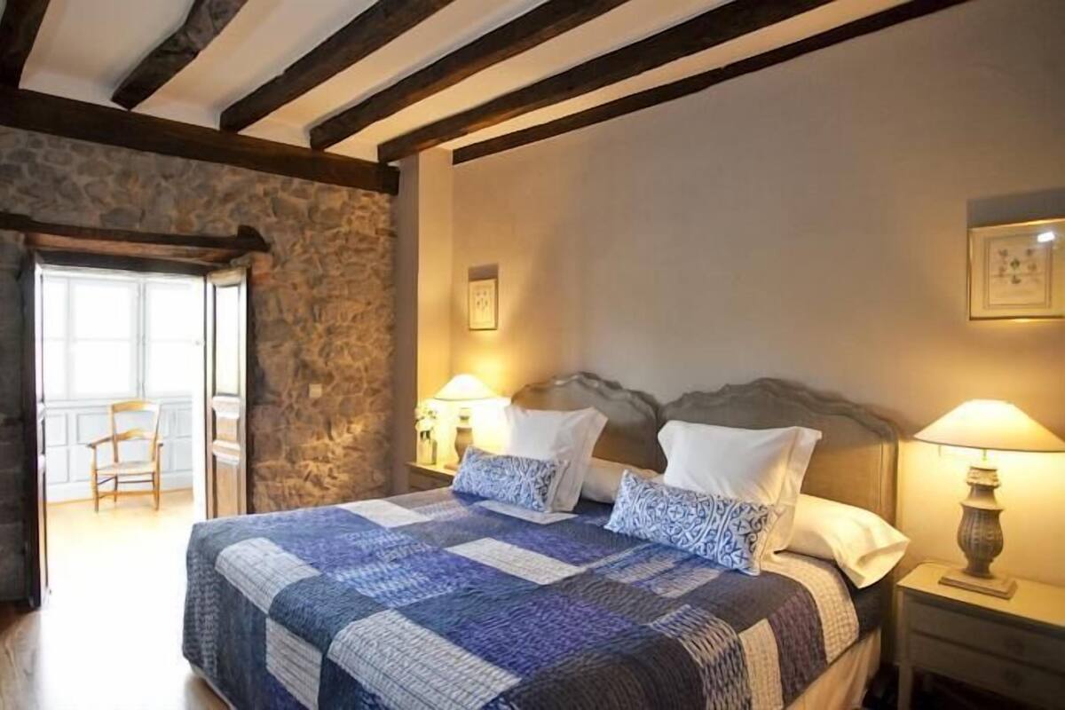 Ein Schlafzimmer mit Stewand, einem hölzernen Bett mit Steppdecke, zwei Nachttischlampen und einem Sessel.