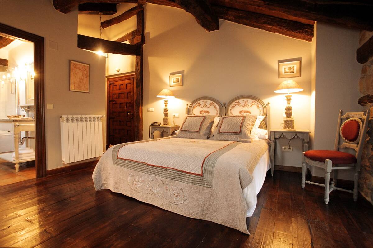 Ein traditionell eingerichtetes Schlafzimmer mit einem großen Bett, zwei Nachttischen mit Lampen, einem Holzstuhl und einer Steinwand.