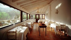 A dining area with wooden beams, white tables, and chairs, large windows with a view of greenery. - Hotel Casona de Quintana (Soba)
