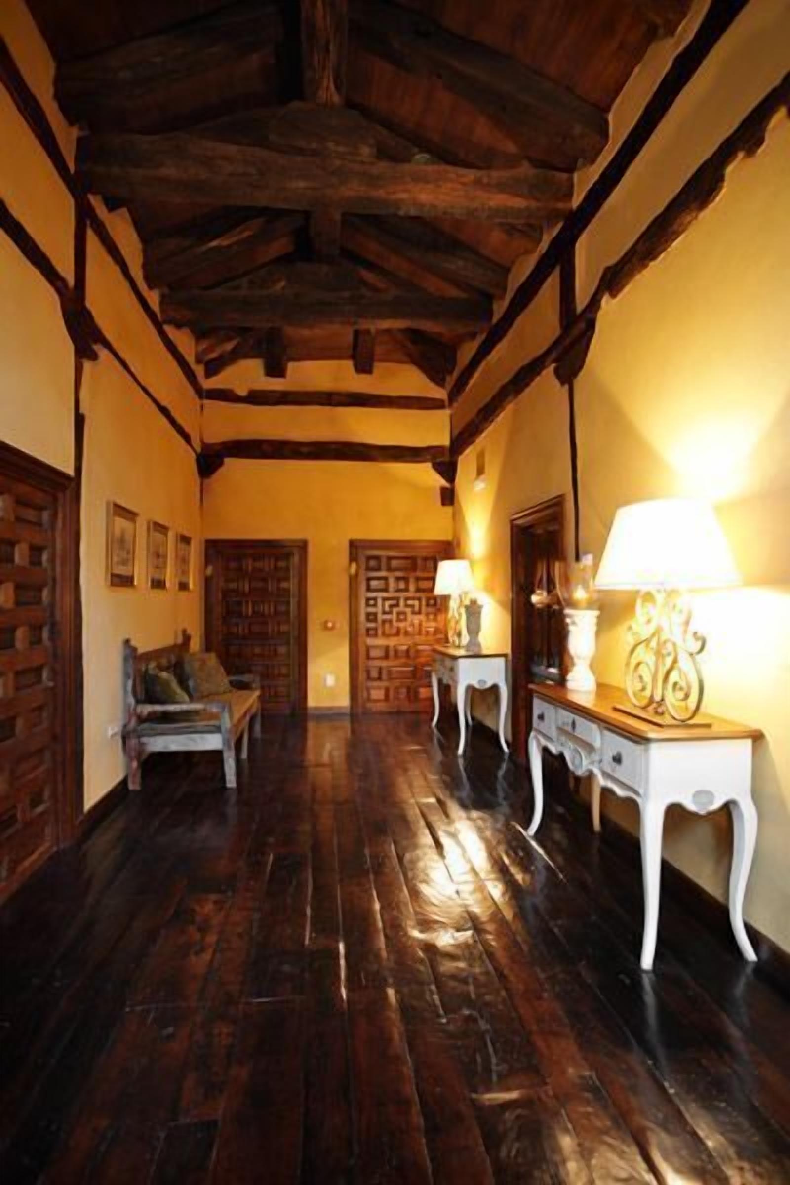 A hallway with wooden flooring, a bench, and two tables with lamps.