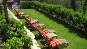 A patio with wooden lounge chairs and tables, surrounded by a well-maintained lawn and hedges. - Hotel Casona de Quintana (Soba)