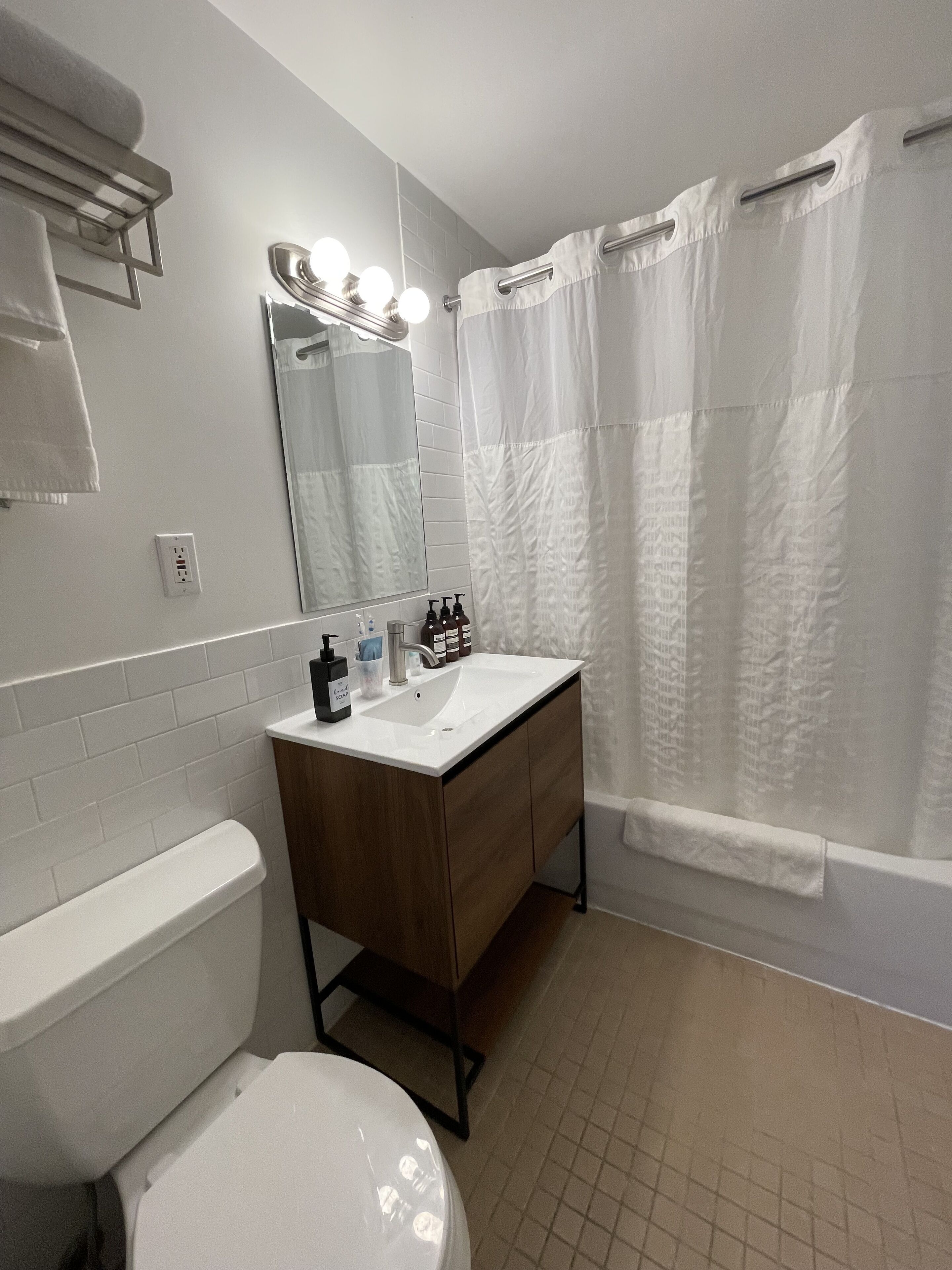 Un bany amb un vàter blanc, un lavabo amb un mirall damunt i una cortina de bany.
