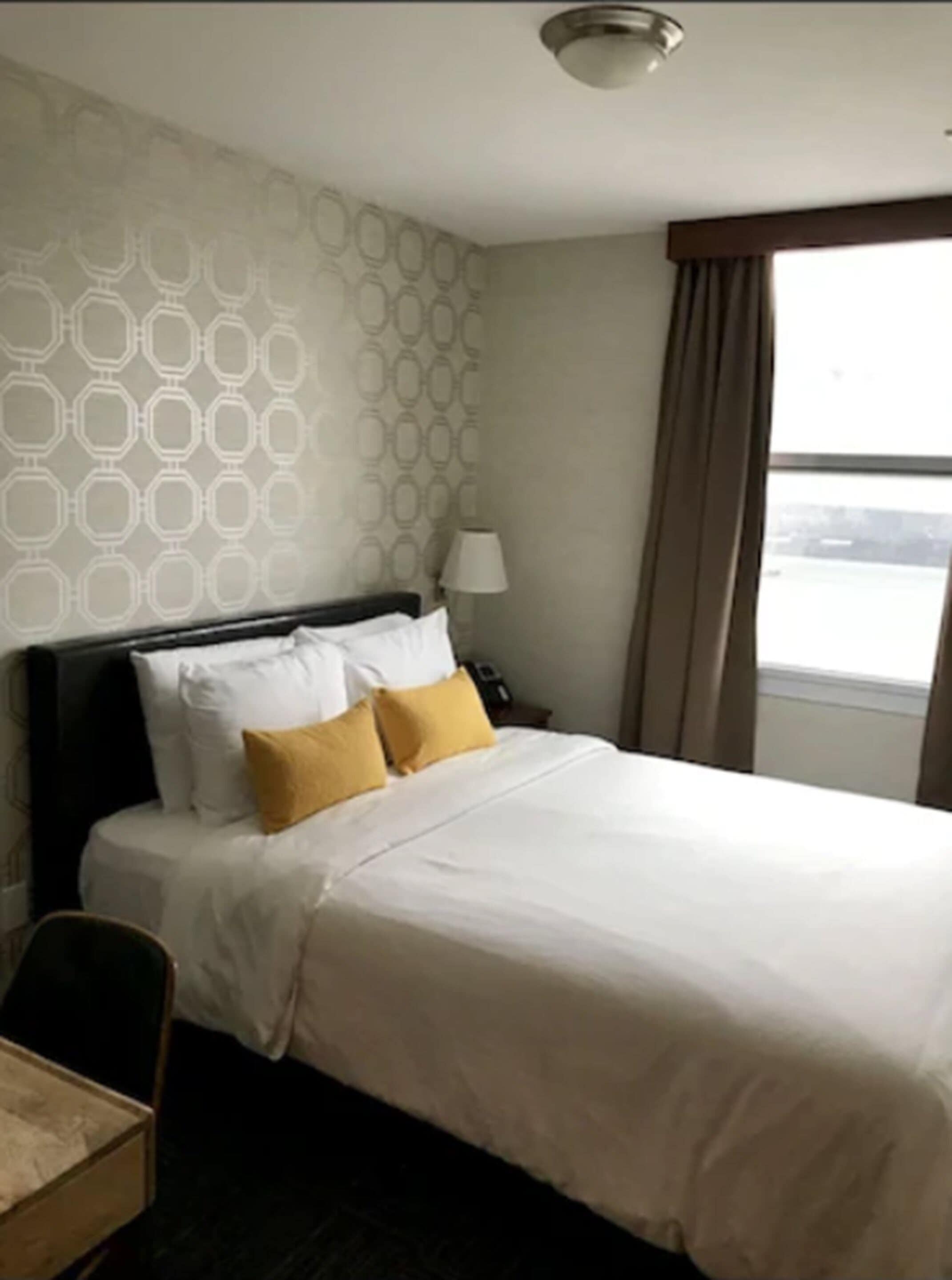 A hotel room with a bed, a nightstand, a lamp, and a window with curtains.