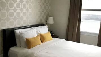 A hotel room with a bed, a nightstand, a lamp, and a window with curtains.