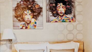 A hotel room with a bed, two pillows, a bedside table with a lamp, and two wall art pieces.