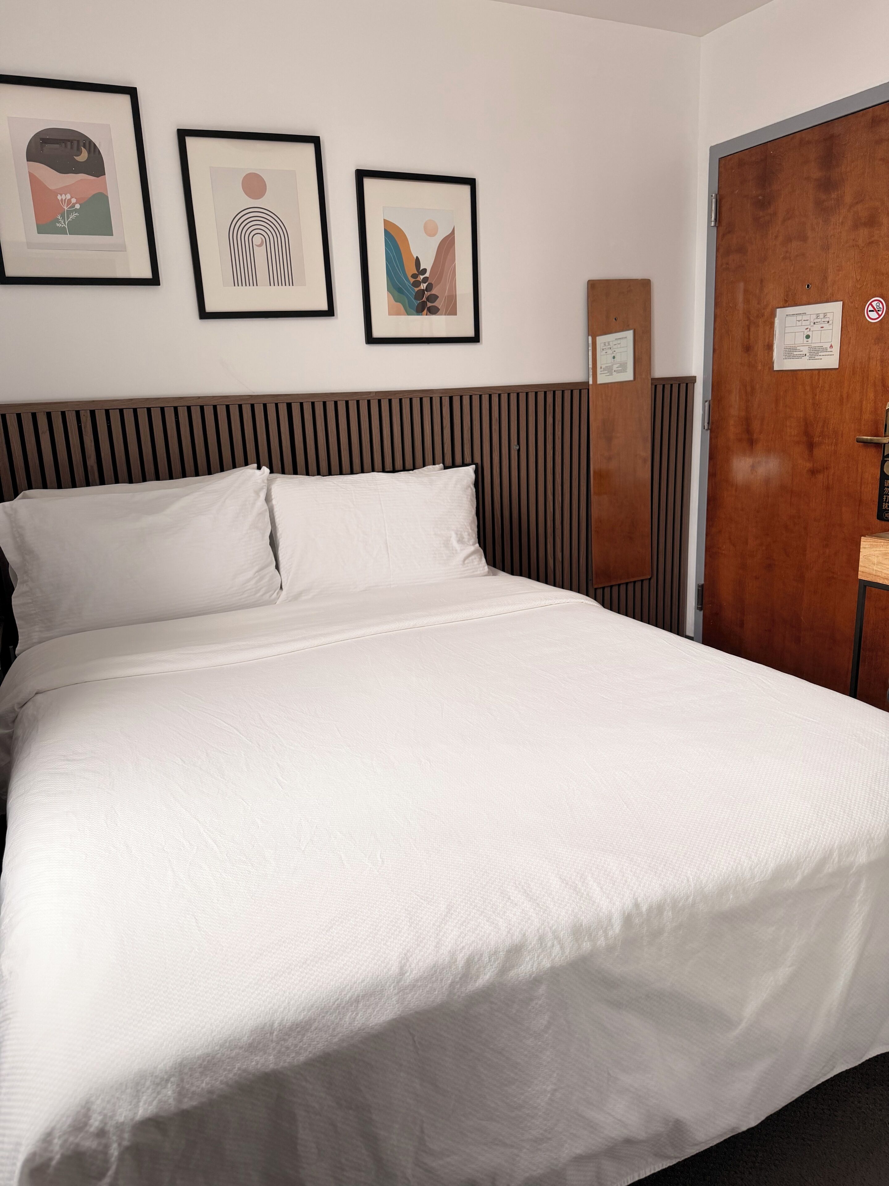 Una habitació d'hotel amb un llit, un panell de capçalera de fusta i tres quadres al mur.