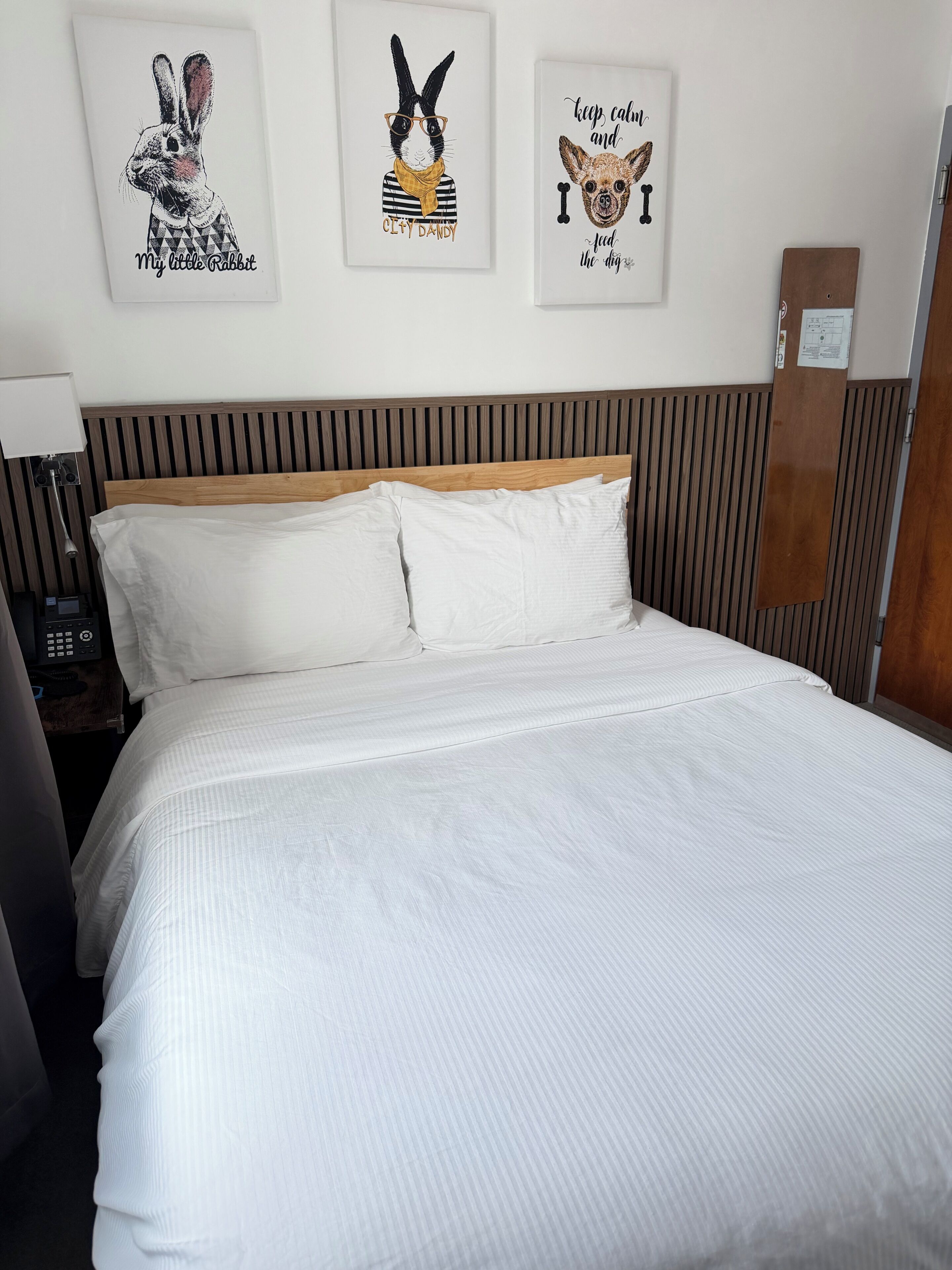 Una cama bien hecha con sábanas blancas, un cabecero de madera y tres cuadros en la pared superior.