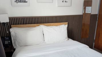 Una cama bien hecha con sábanas blancas, un cabecero de madera y tres cuadros en la pared superior.