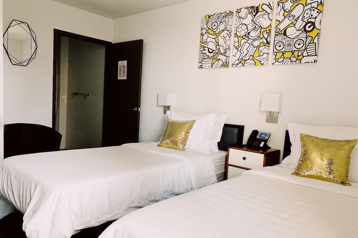 A hotel room with two beds, a desk, a chair, and artwork on the wall.